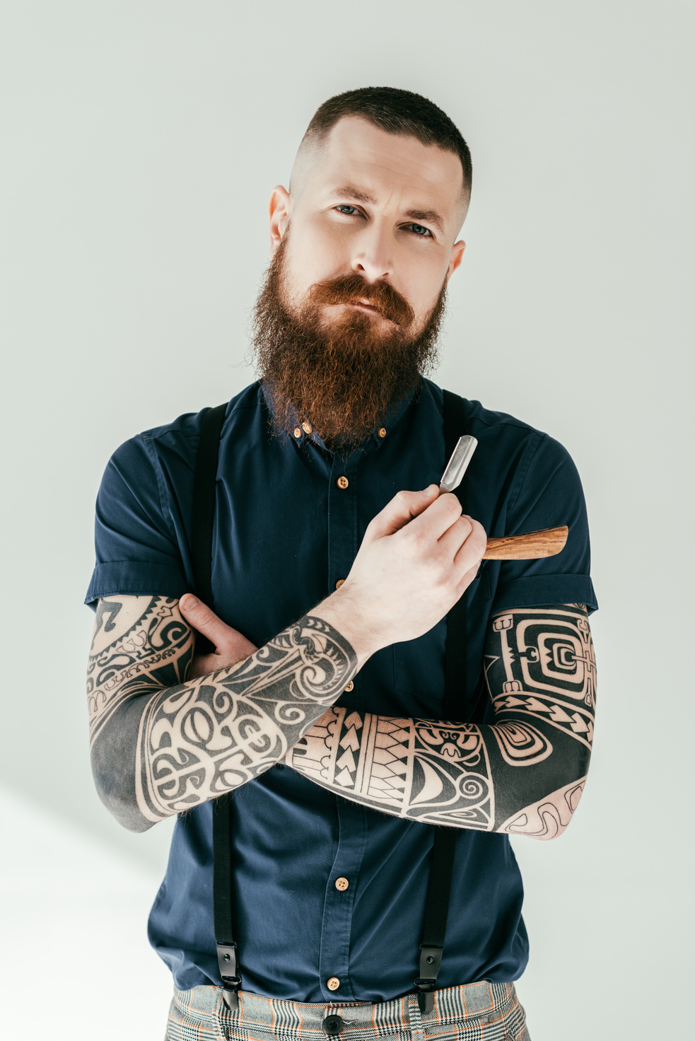handsome tattooed man holding razor and looking at camera